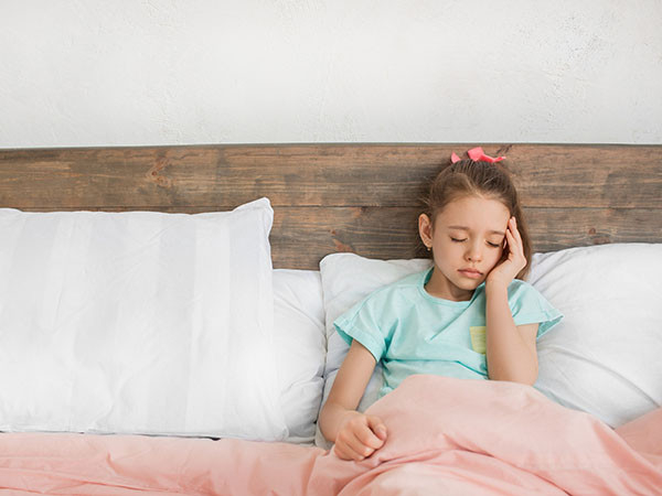 photo of a tween girl in bed with her back against pillows, looking ill and holding her left hand to the side of her face
